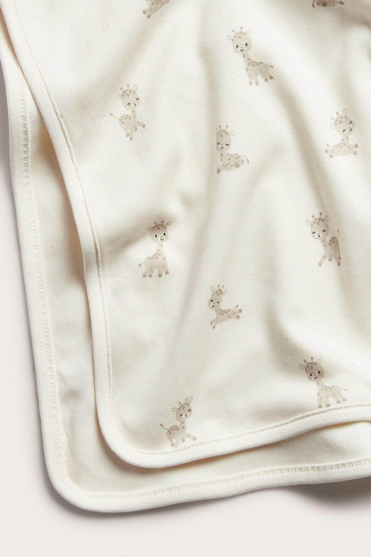 Zbliżenie złożonego, jasnobeżowego kocyka niemowlęcego z bawełny interlock w powtarzający się wzór żyraf.