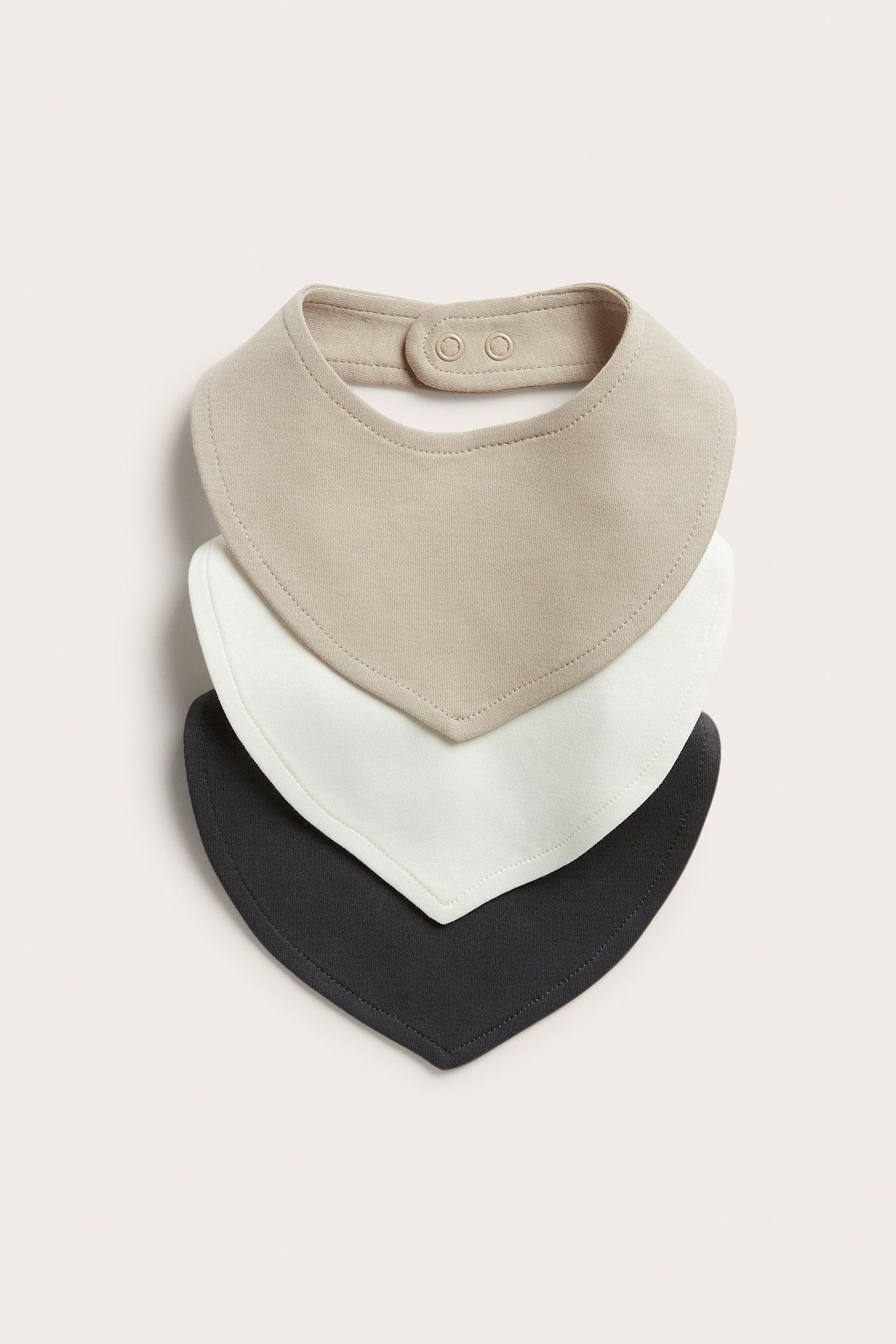 Widok z przodu 3-paku bawełnianych śliniaków dla niemowląt w beżu, bieli i czerni, z napami.