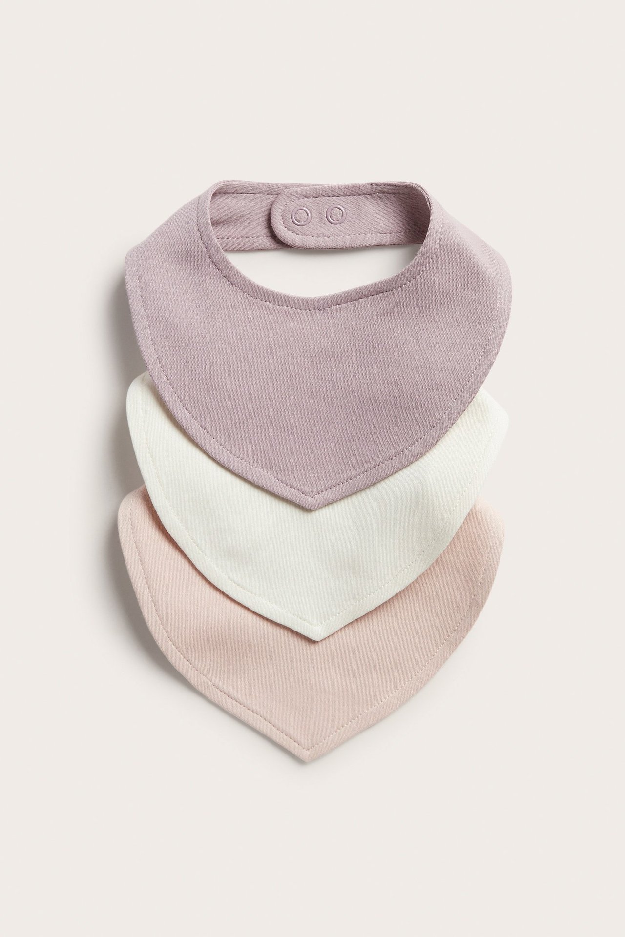 Edestäpäin: Kolme pinottua puuvillalappua: violetti, luonnonvalkoinen ja vaaleanpunainen, neppareilla.