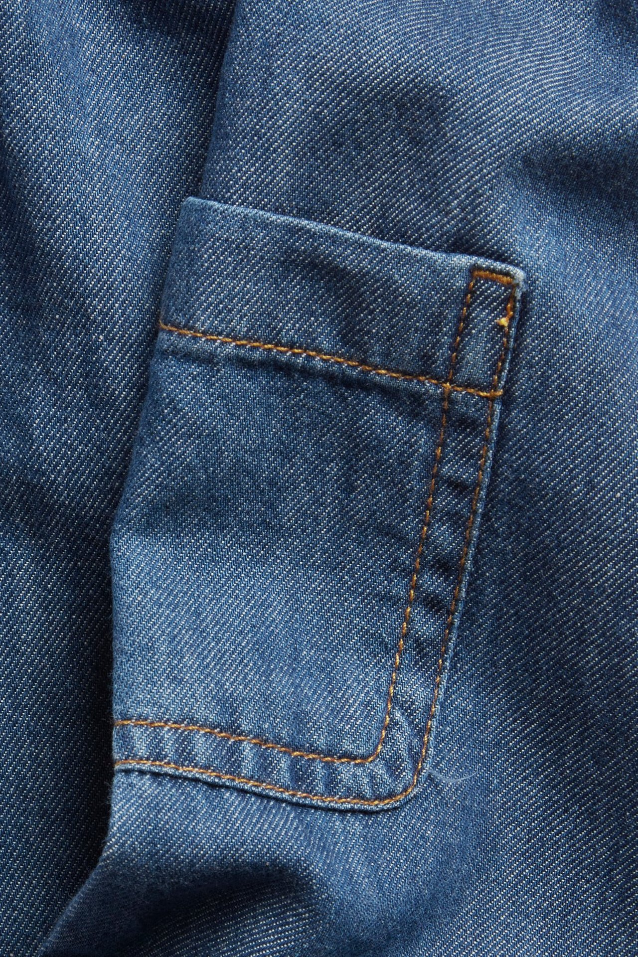 Nærbilde av mørkeblå denim babybukser med sidelomme og oransje sømmer.