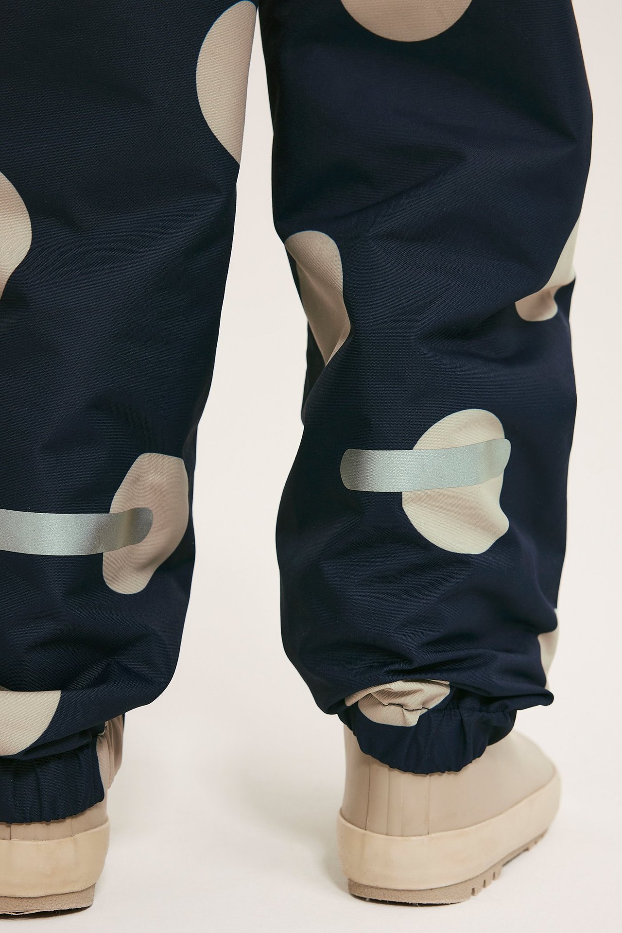 Forfra: Barns mørkeblå prikkete skallbukse med refleksdetaljer og beige støvler.