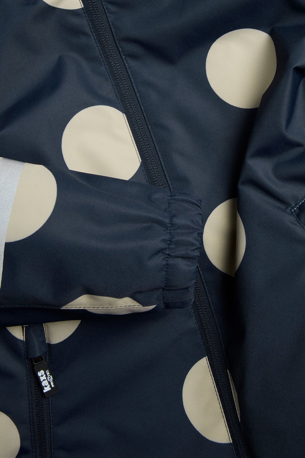 Närbild av en mörkblå barnskaljacka med beiga prickar, svart dragkedja och resårmudd.