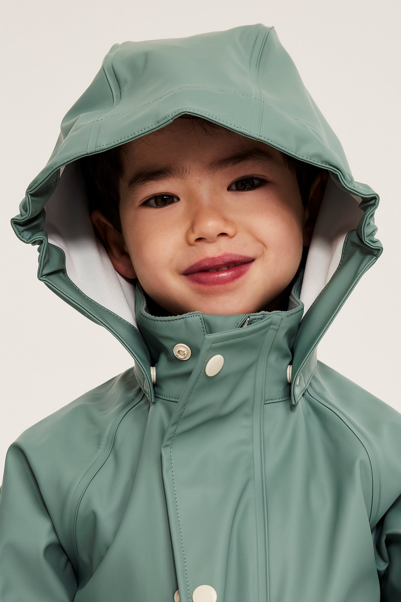 Närbild, framifrån, på ett barn i en ljusgrön regnjacka med huva, dragkedja och tryckknappar.