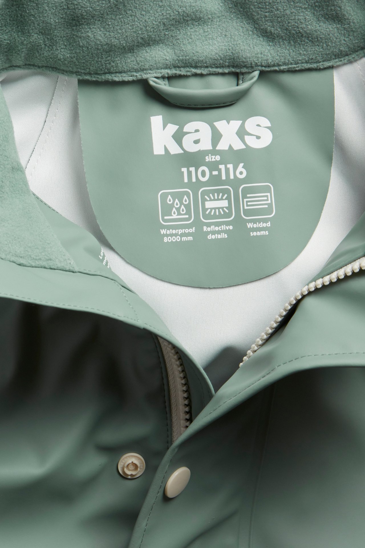 Närbild på en ljusgrön regnjacka för barn med dragkedja, tryckknappar och inneretikett.