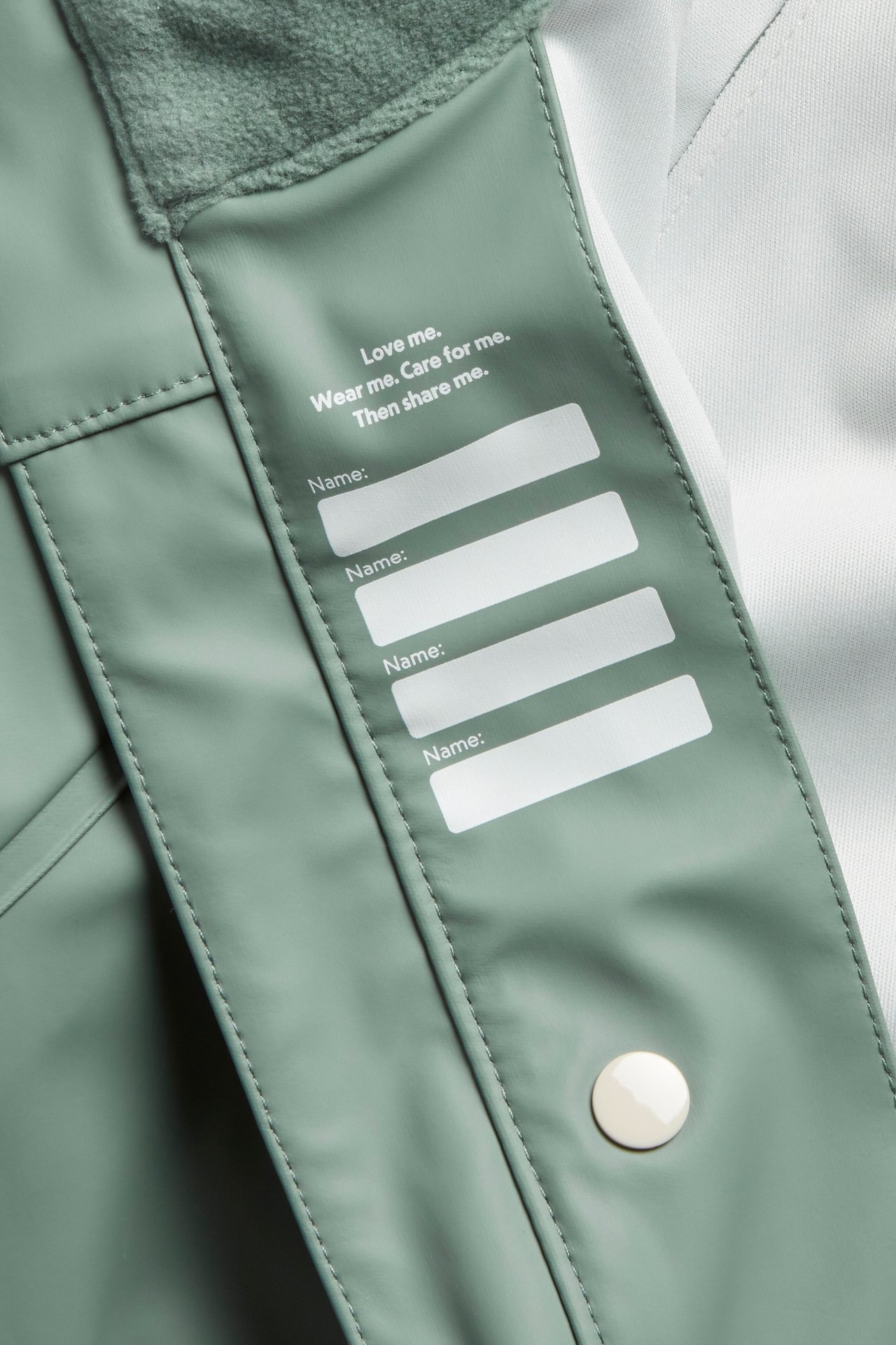 Närbild av en ljusgrön regnjackas insida, med namnlapp och en vit tryckknapp.