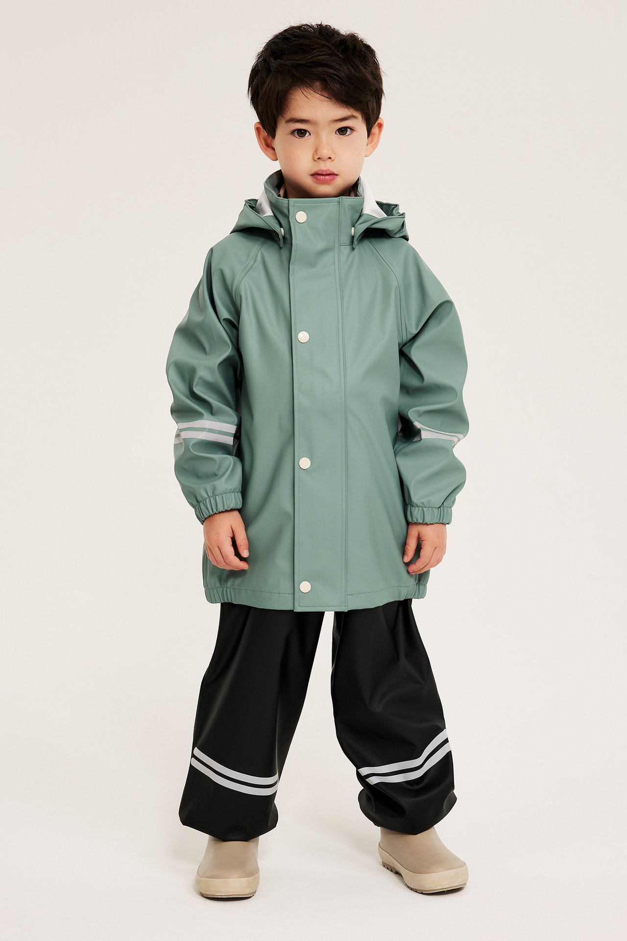 Frontvy av ett barn i ljusgrön regnjacka med reflexer och svarta regnbyxor.