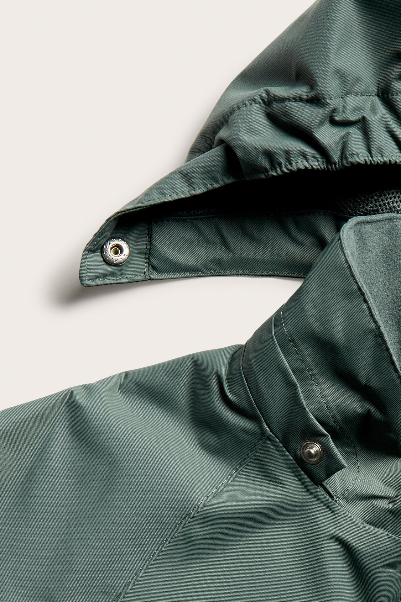 Närbild på khakigrön vattentät skaljacka med fleecefodrad krage och luva med tryckknapp.