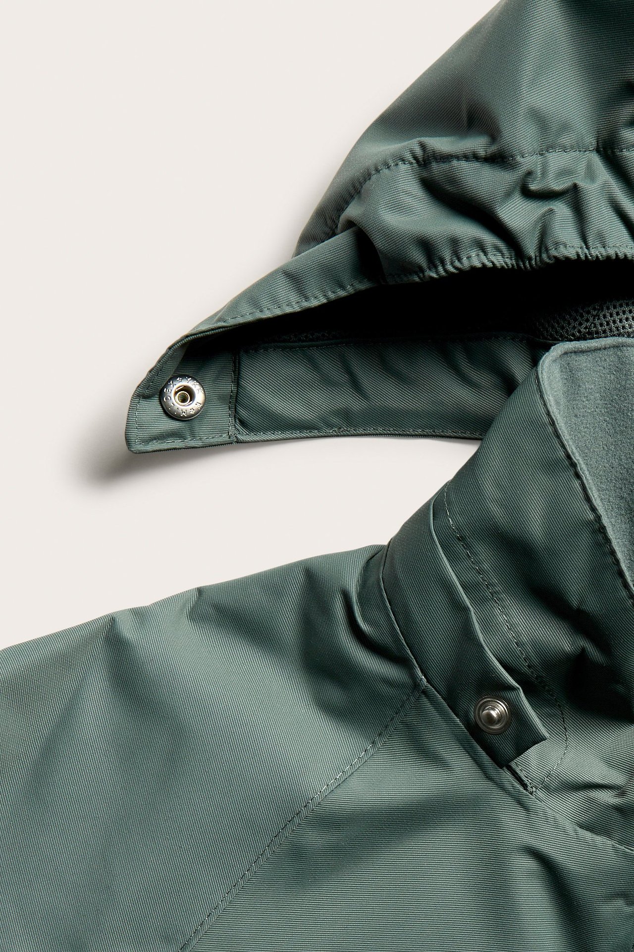 Zbliżenie na zieloną wodoodporną kurtkę shell z polarowym kołnierzem i kapturem na zatrzaski.