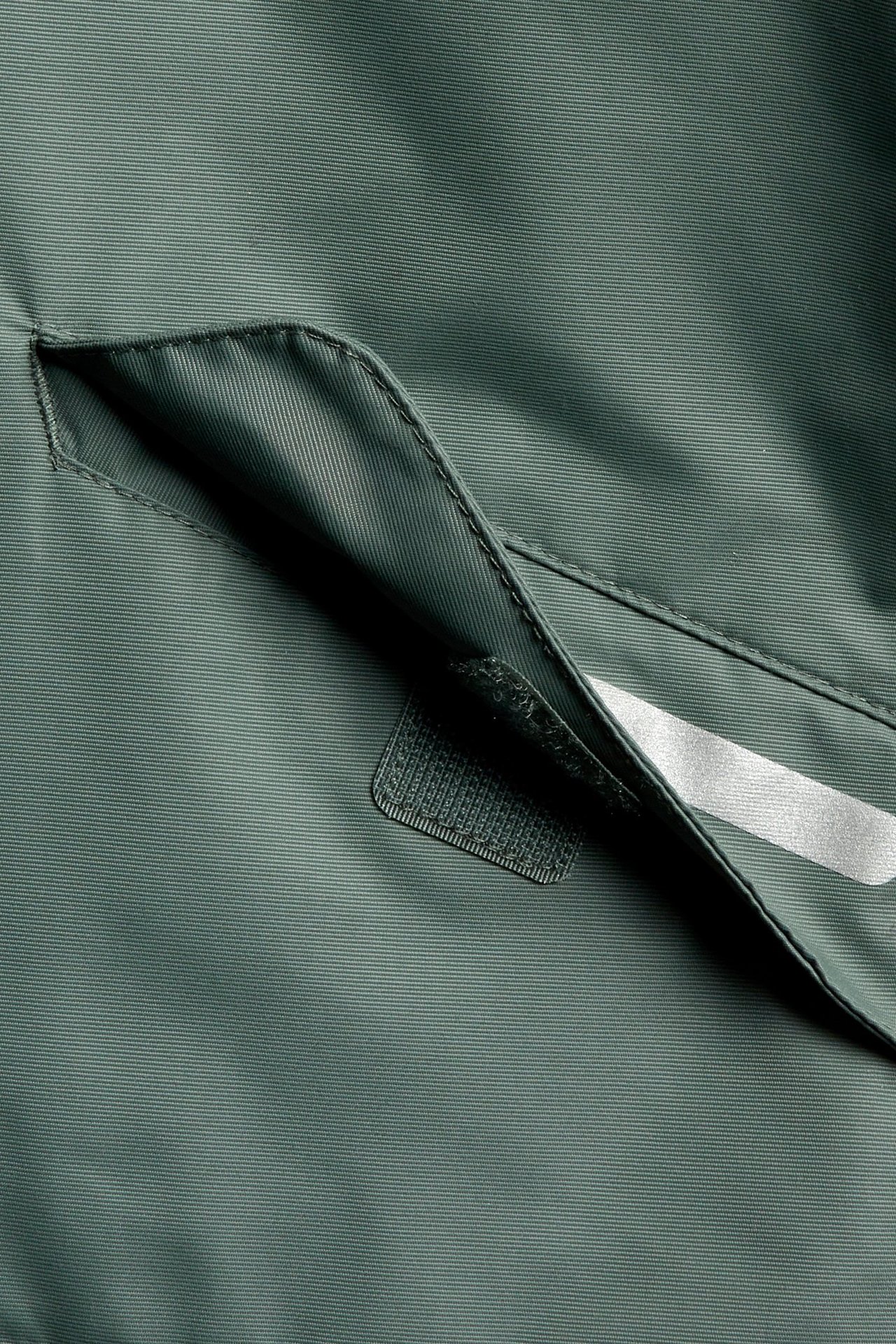 Närbild av en khakigrön vattentät skaljackas ficka med reflekterande band och kardborreförslutning.