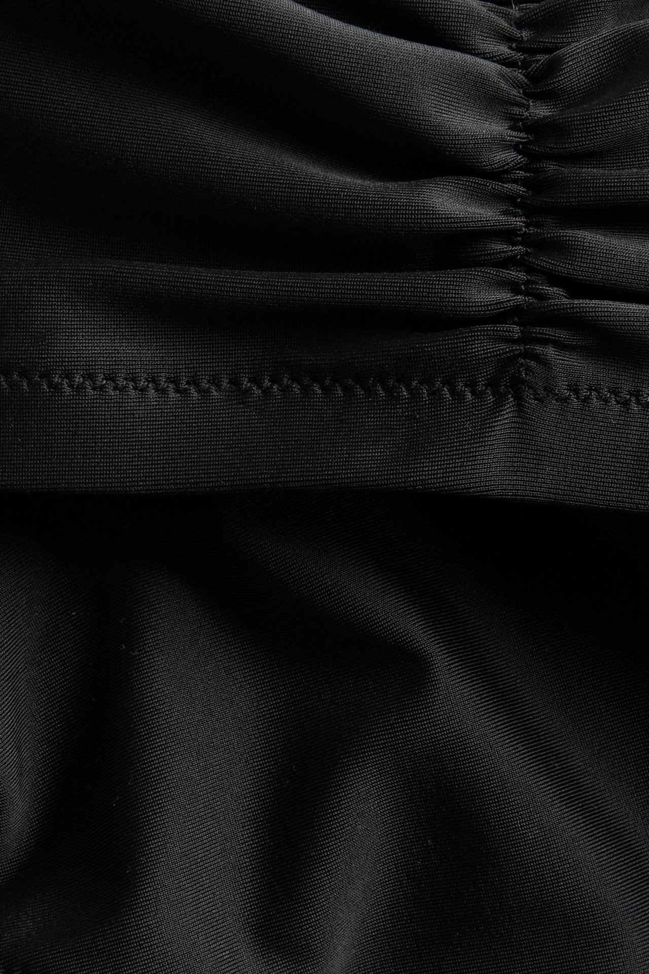 Zbliżenie czarnego topu bikini z marszczonym detalem i widocznymi szwami.
