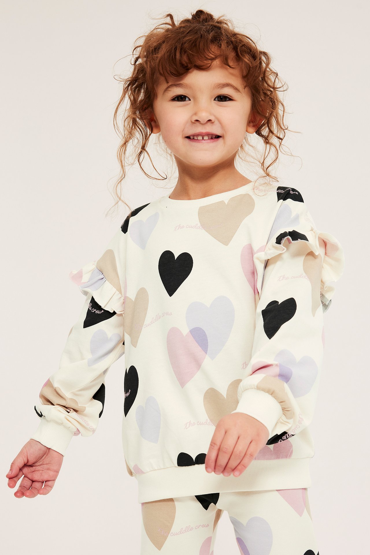 Widok z przodu: Dziecko w kremowej bluzie bawełnianej z serduszkami, falbankami i pasującymi legginsami.