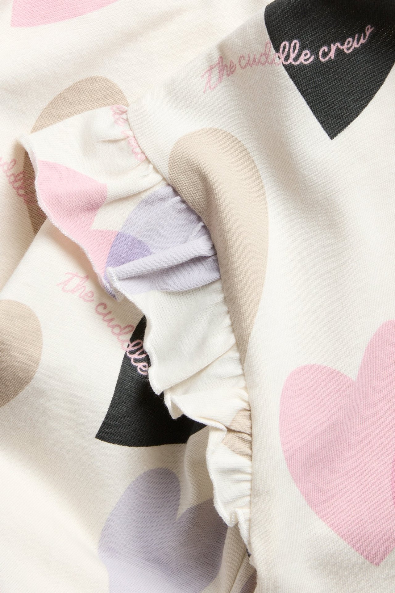 Zbliżenie na kremową bawełnianą bluzę z wielokolorowym nadrukiem serc i falbanką na rękawie.