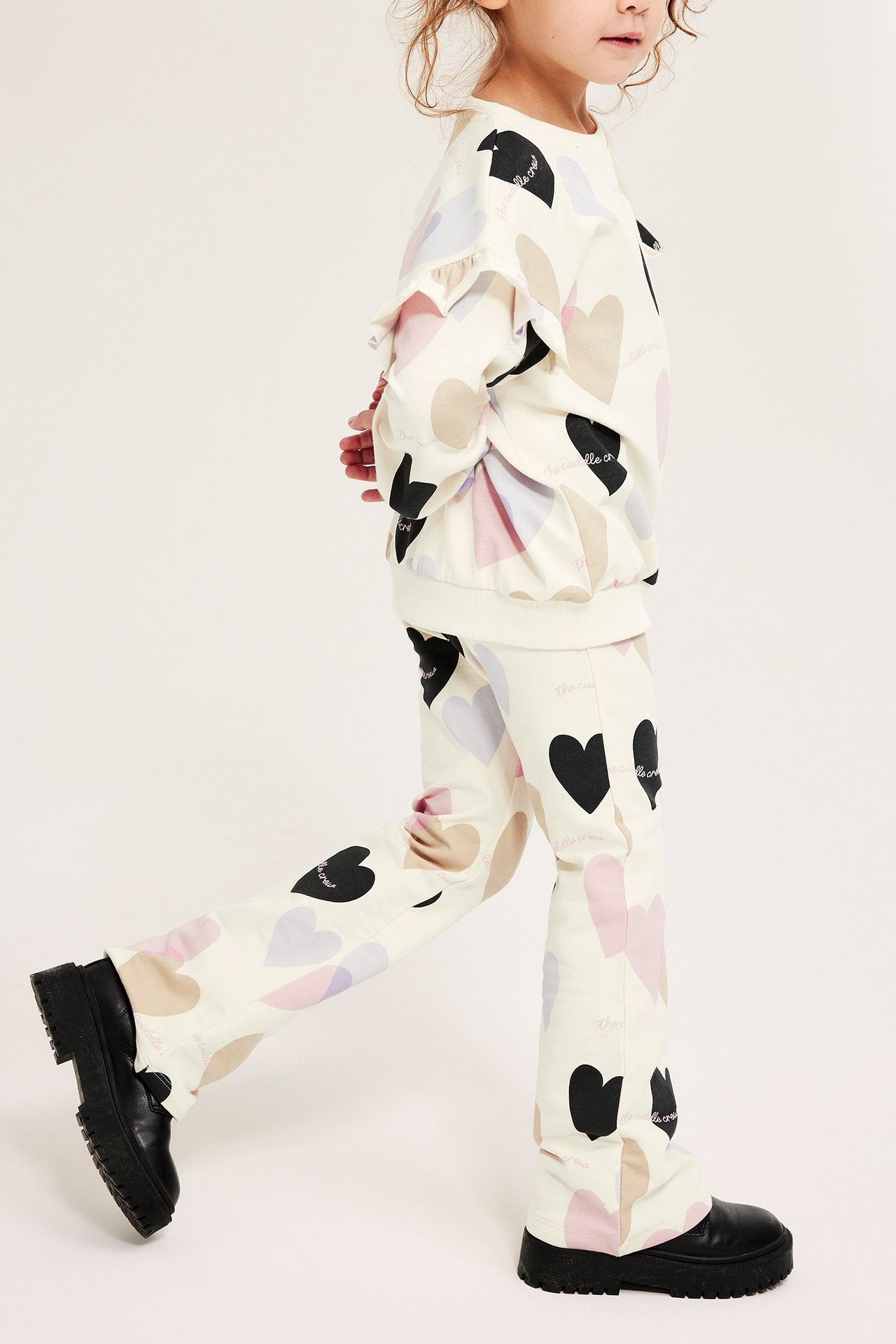 Sidovy av ett barn i off-white ribbade utsvängda leggings med hjärtmönster och matchande långärmad topp.