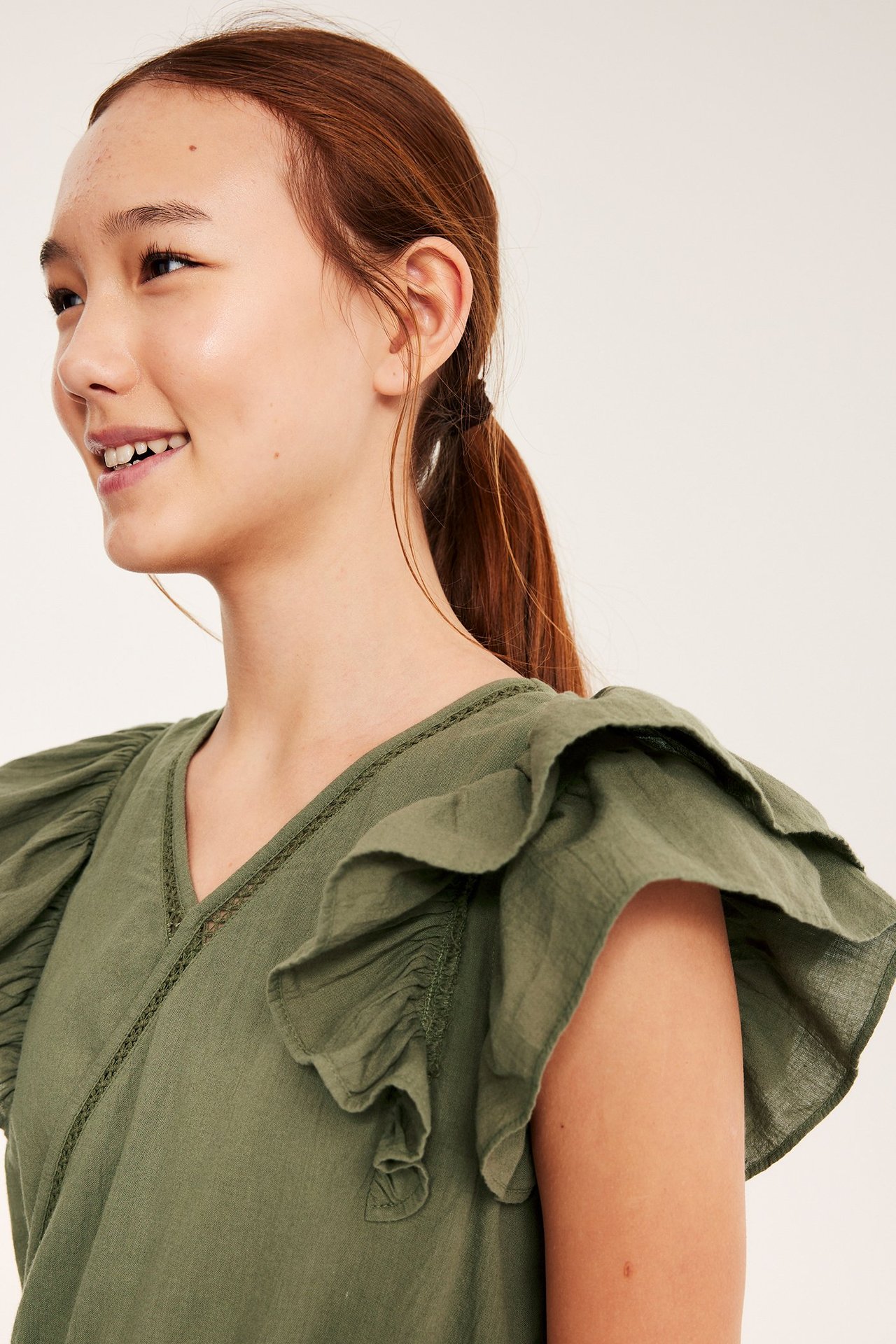 Zbliżenie, widok z boku dziecka w ciemnozielonej bawełnianej sukience z falbanami i koronkowymi detalami.