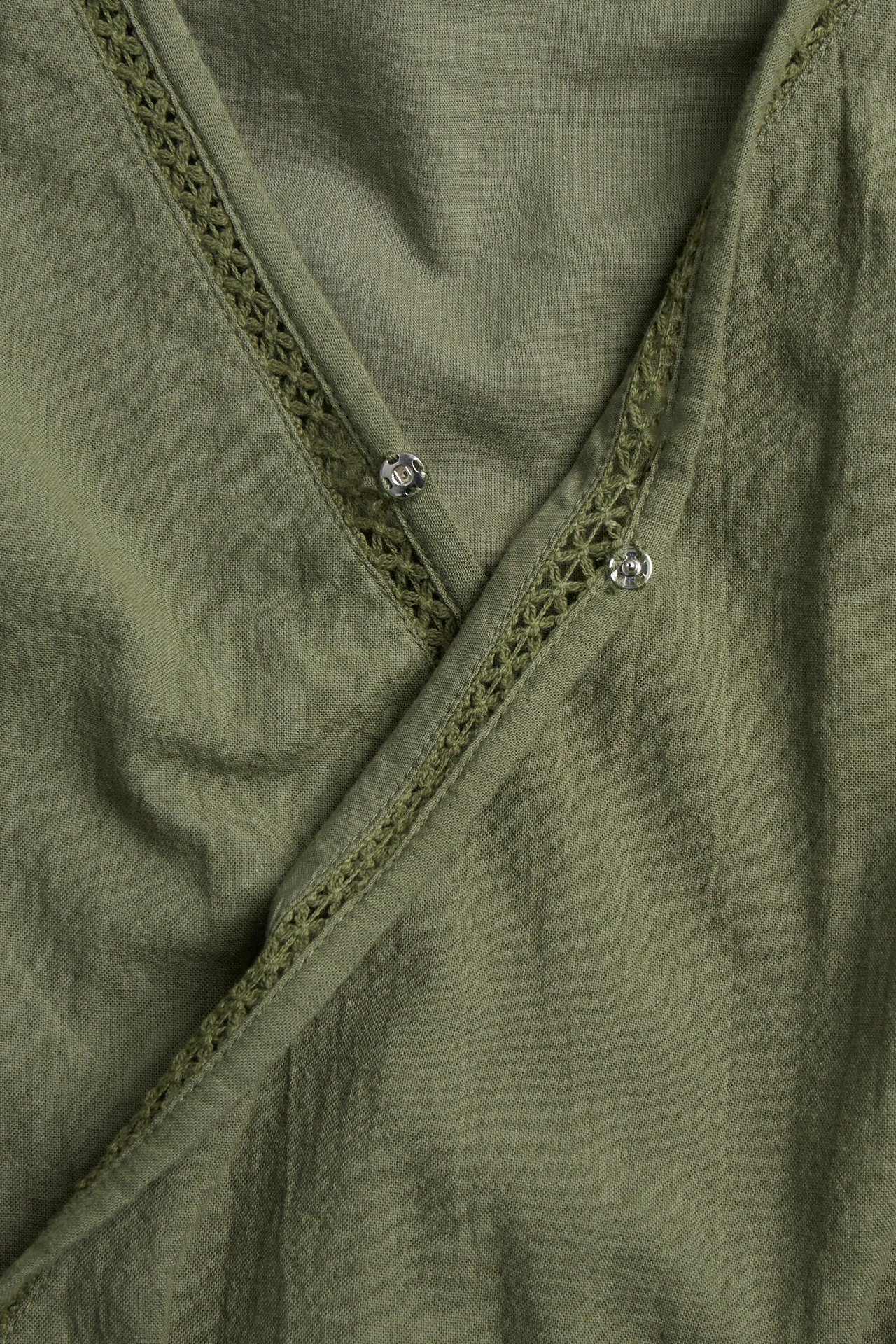 Zbliżenie ciemnozielonej bawełnianej sukienki z dekoltem kopertowym, koronkowymi wstawkami i zatrzaskami.