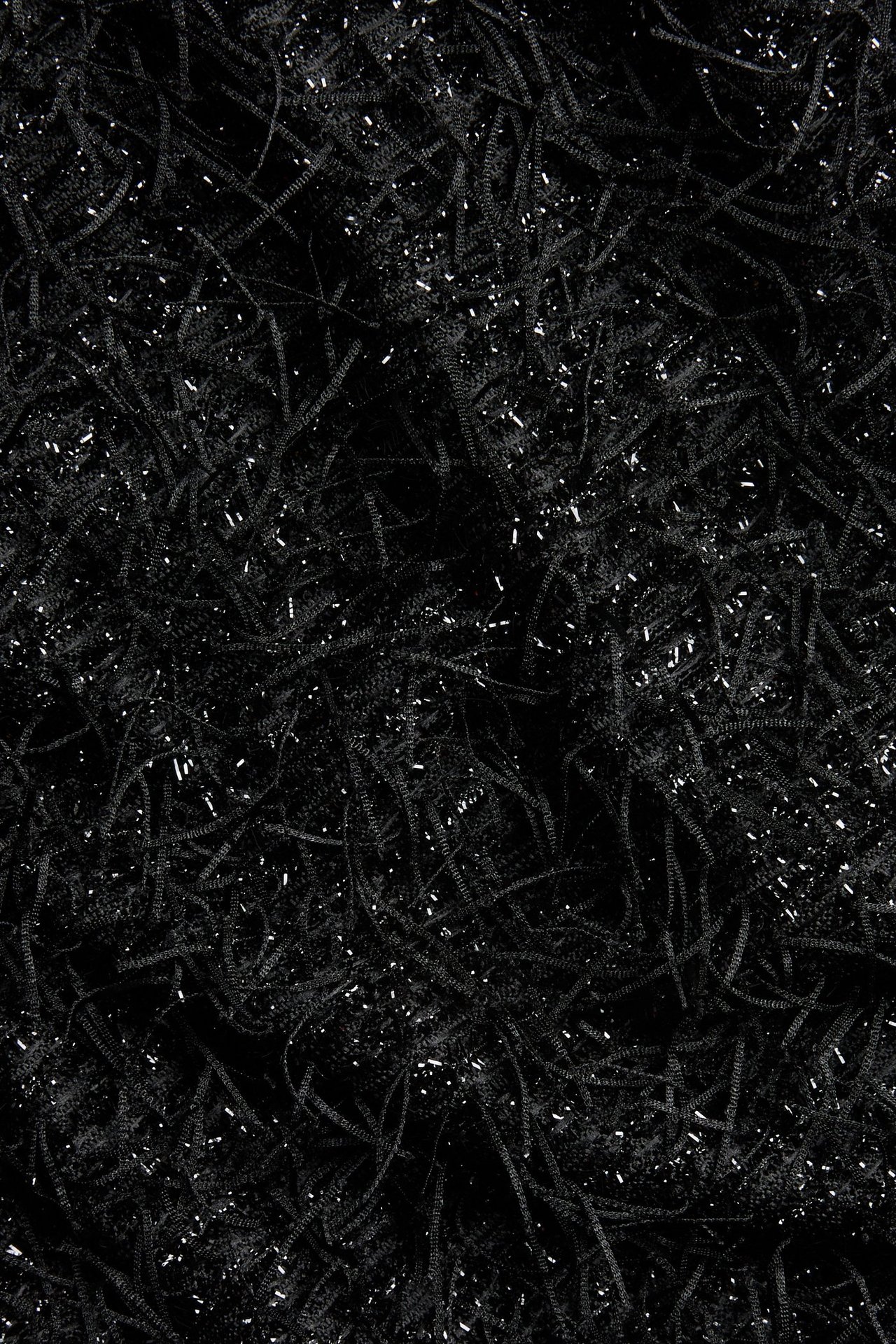 Zbliżenie czarnego, teksturowanego materiału na krótki top, z małymi błyszczącymi frędzlami.