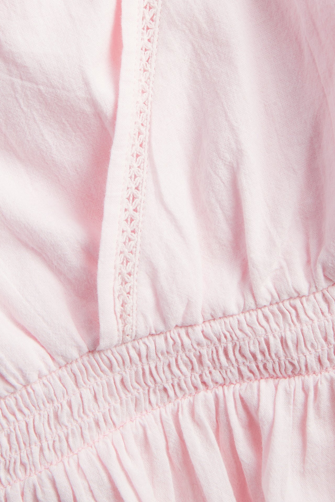 Närbild på ljusrosa volangblus i bomull med spetsdetaljer och smock i midjan.