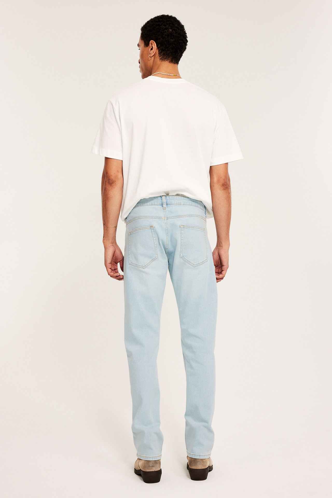 Mies, takaa, yllään vaaleansiniset regular fit -farkut, valkoinen t-paita ja beiget kengät.