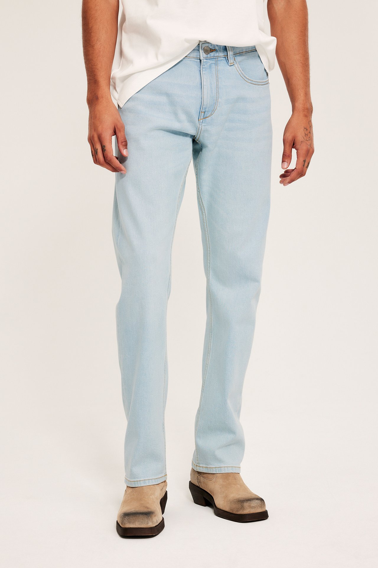 Framifrån, en man i ljusblå regular fit jeans, stylade med en vit t-shirt och ljusbruna skor.