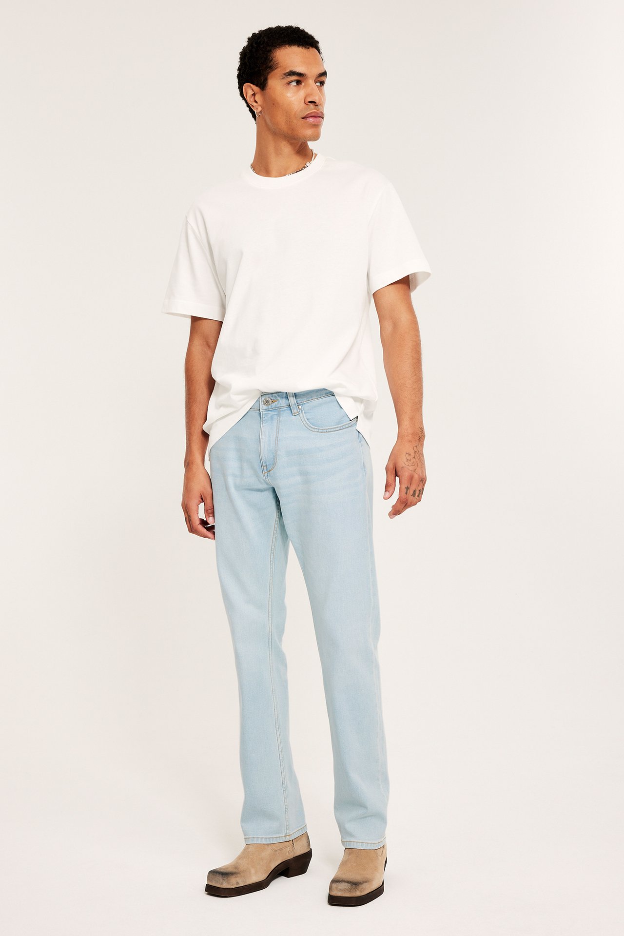 Mężczyzna w jasnoniebieskich jeansach regular fit, białym t-shircie i beżowych butach, przodem.
