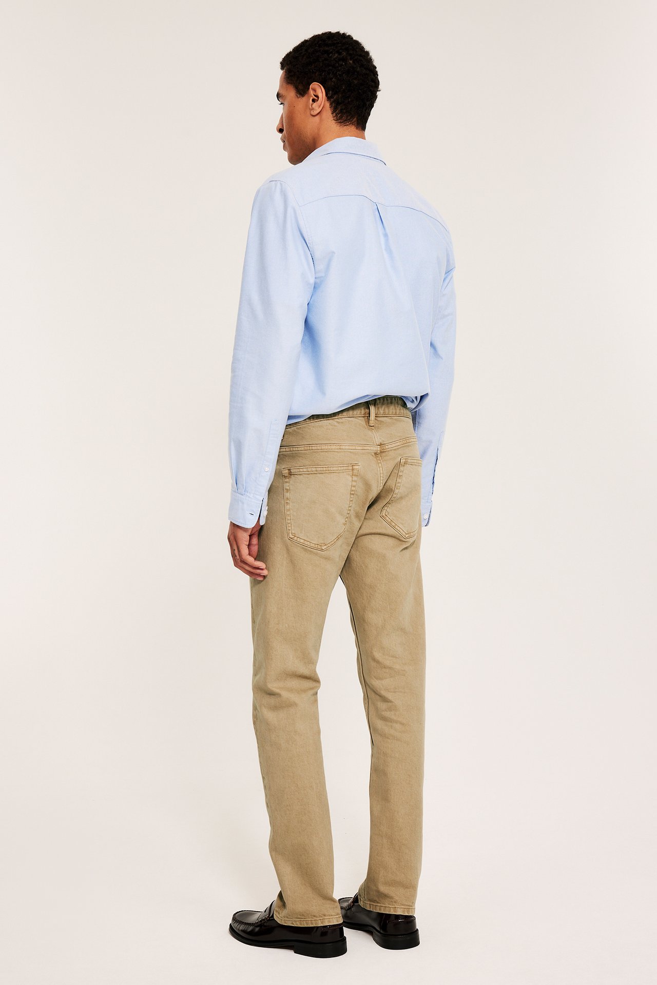 Mies takaa-sivulta: beiget regular fit twillfarkut, vaaleansininen paita ja tummat loaferit.