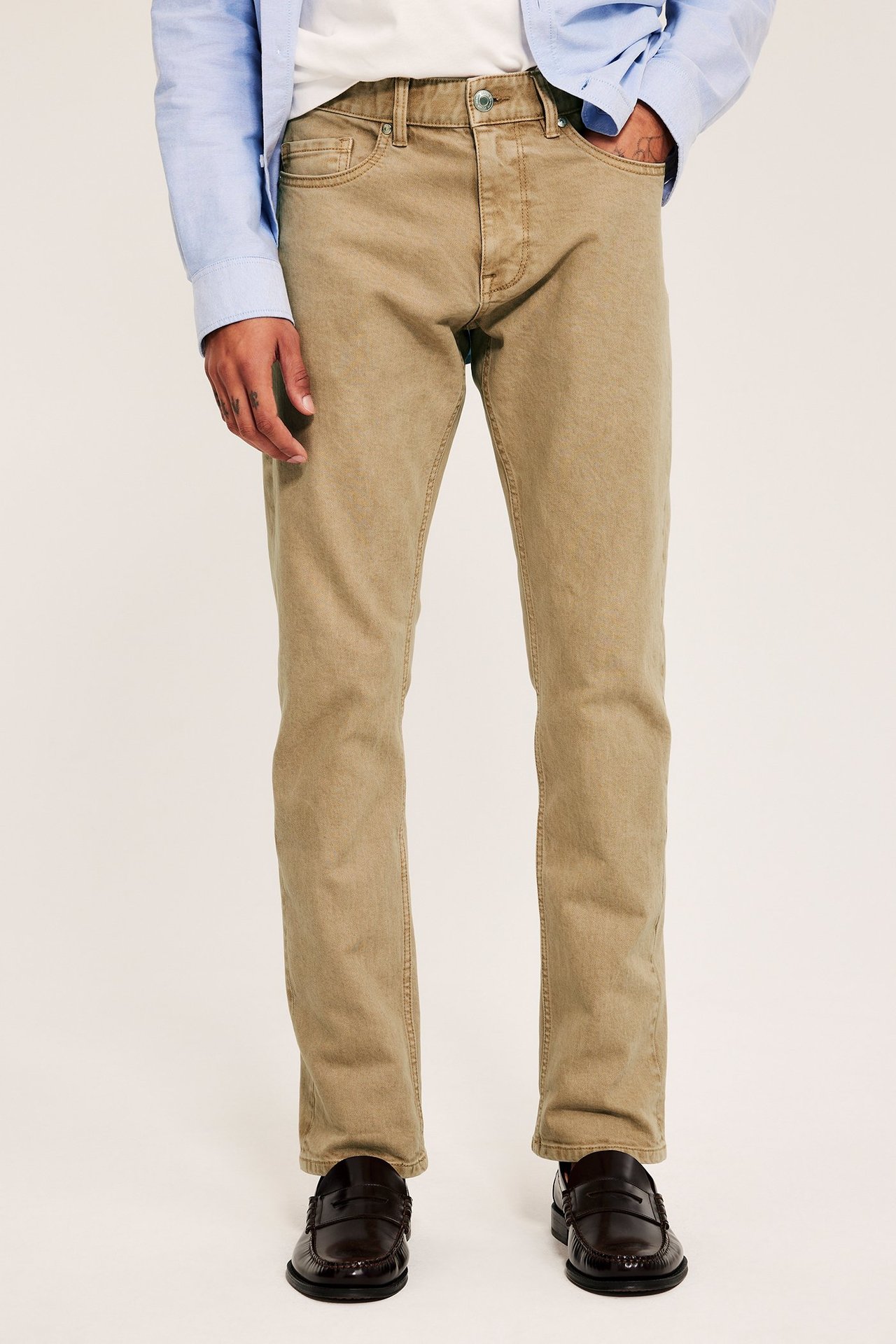 Framsida: man bär beiga regular fit twilljeans, vit t-shirt, ljusblå skjorta och bruna loafers.