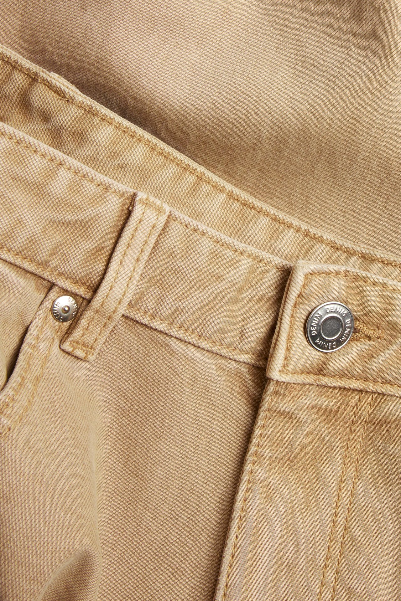 Nærbilde forfra av beige regular twilljeans, som viser en sølvknapp og beltehemper.