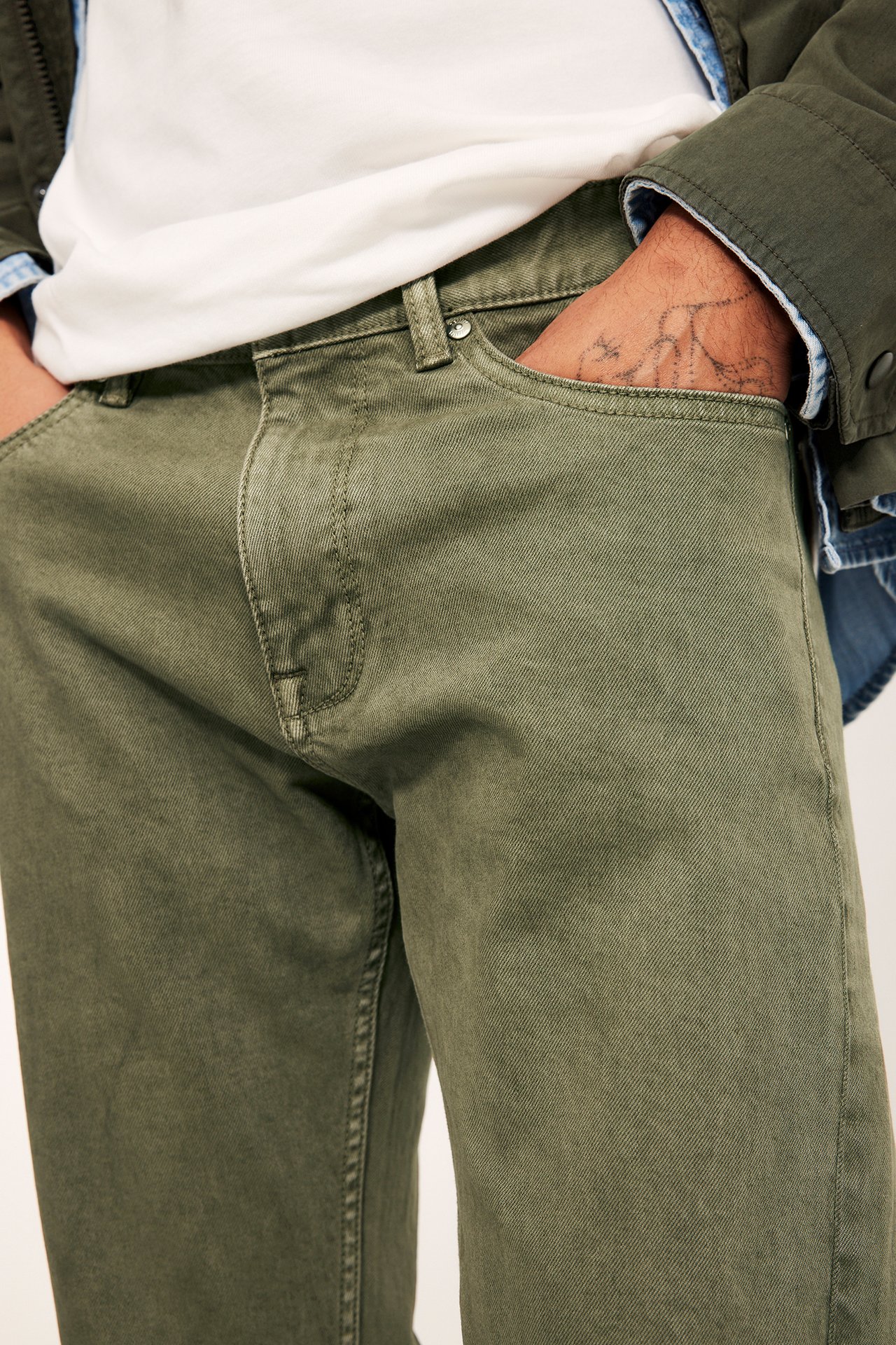Nærbilde forfra av en mann i grønne regular twill-jeans, en hvit T-skjorte og en grønn jakke.