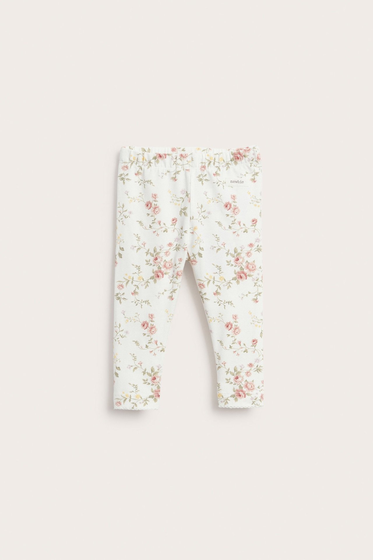 Forfra av off-white baby-leggings med blomstermønster og elastisk midje.