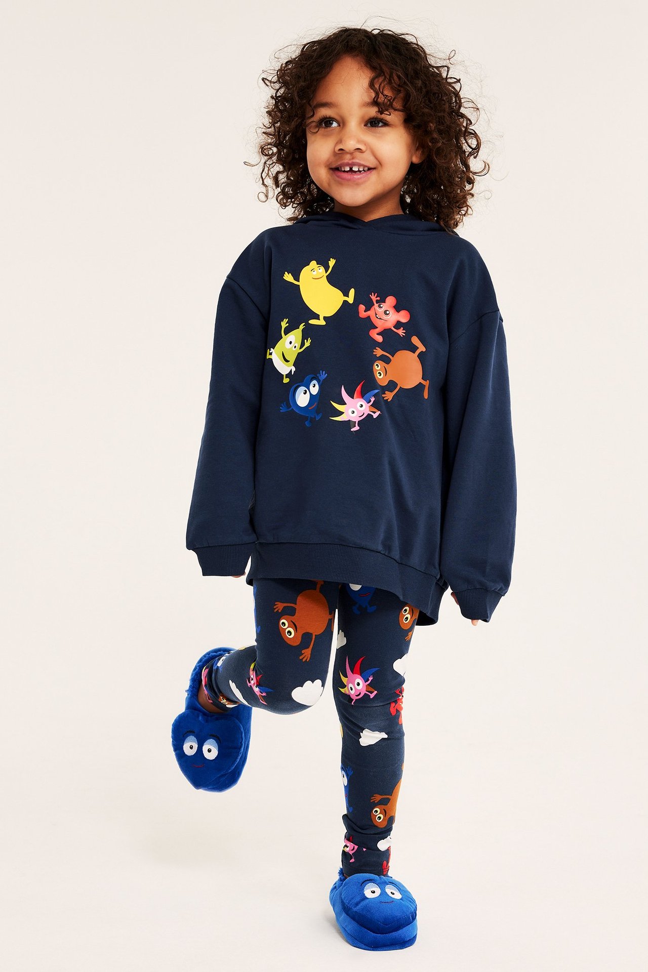 Framifrån: barn i mörkblå mönstrade Babblarna-leggings, huvtröja och blå mjuka tofflor.