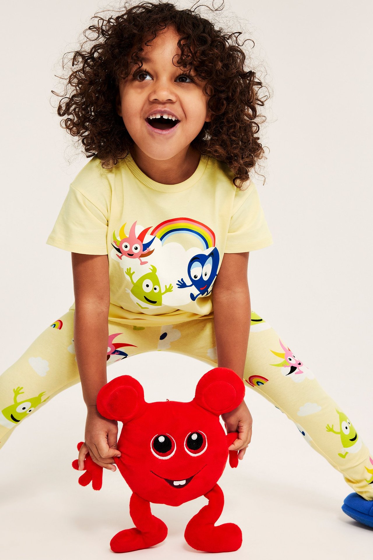 Z przodu: Dziecko w jasnobeżowej bawełnianej koszulce z nadrukiem Babblarna i legginsach, trzyma czerwoną zabawkę.
