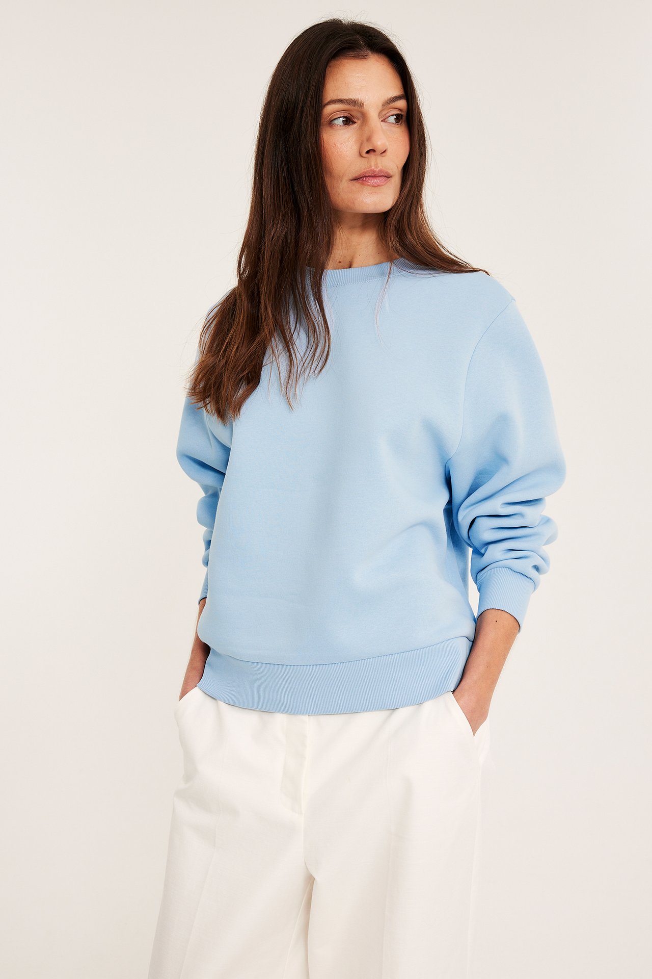 Widok z przodu: kobieta w jasnoniebieskiej bluzie dresowej i białych szerokich spodniach.