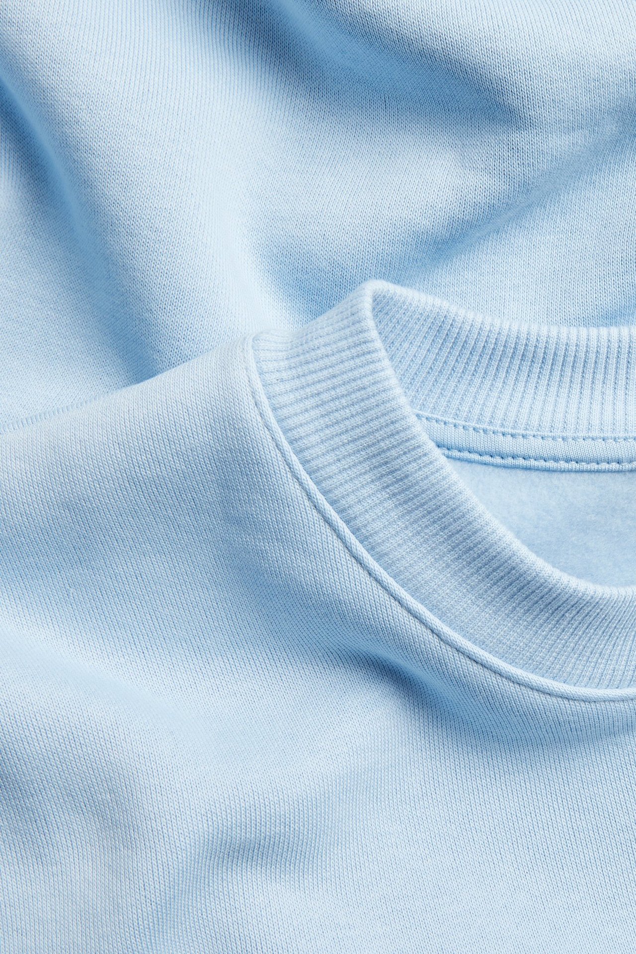 Närbild av en ljusblå bomullsmix sweatshirt med ribbade muddar och halsringning.
