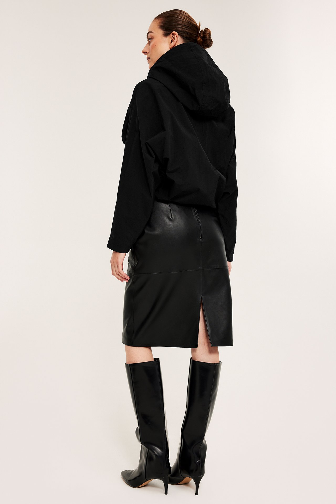 Kobieta od tyłu z lewej w czarnej luźnej kurtce z kapturem, czarnej spódnicy ze sztucznej skóry i czarnych butach.