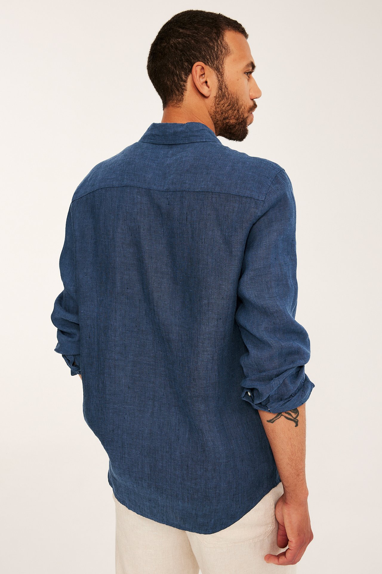 Bakside av mann i mørkeblå melert linskjorte med opprullede ermer og lysebeige bukser.