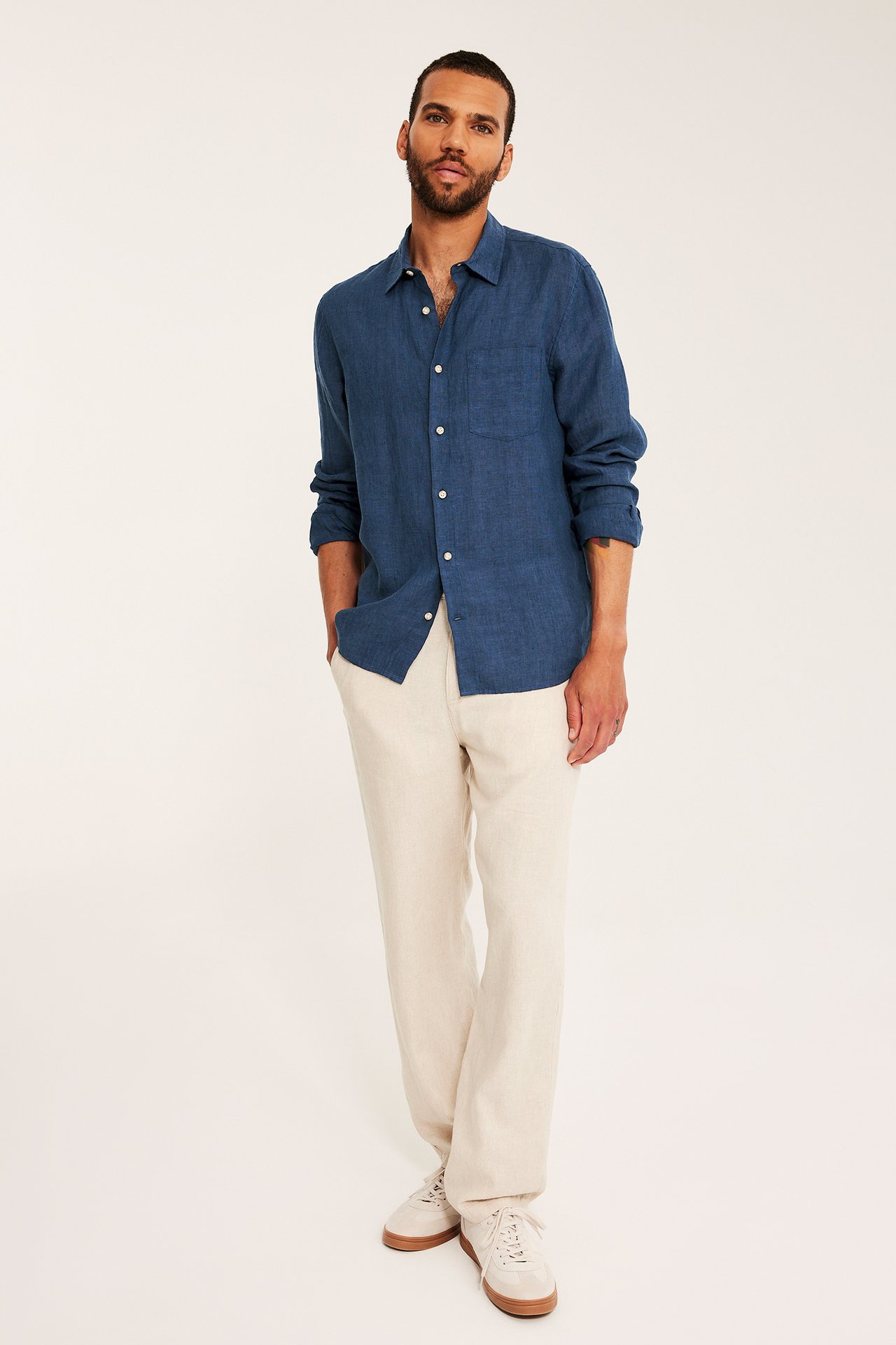 Framifrån, en man i mörkblå melerad linneskjorta, regular fit, ljusbeige byxor och sneakers.