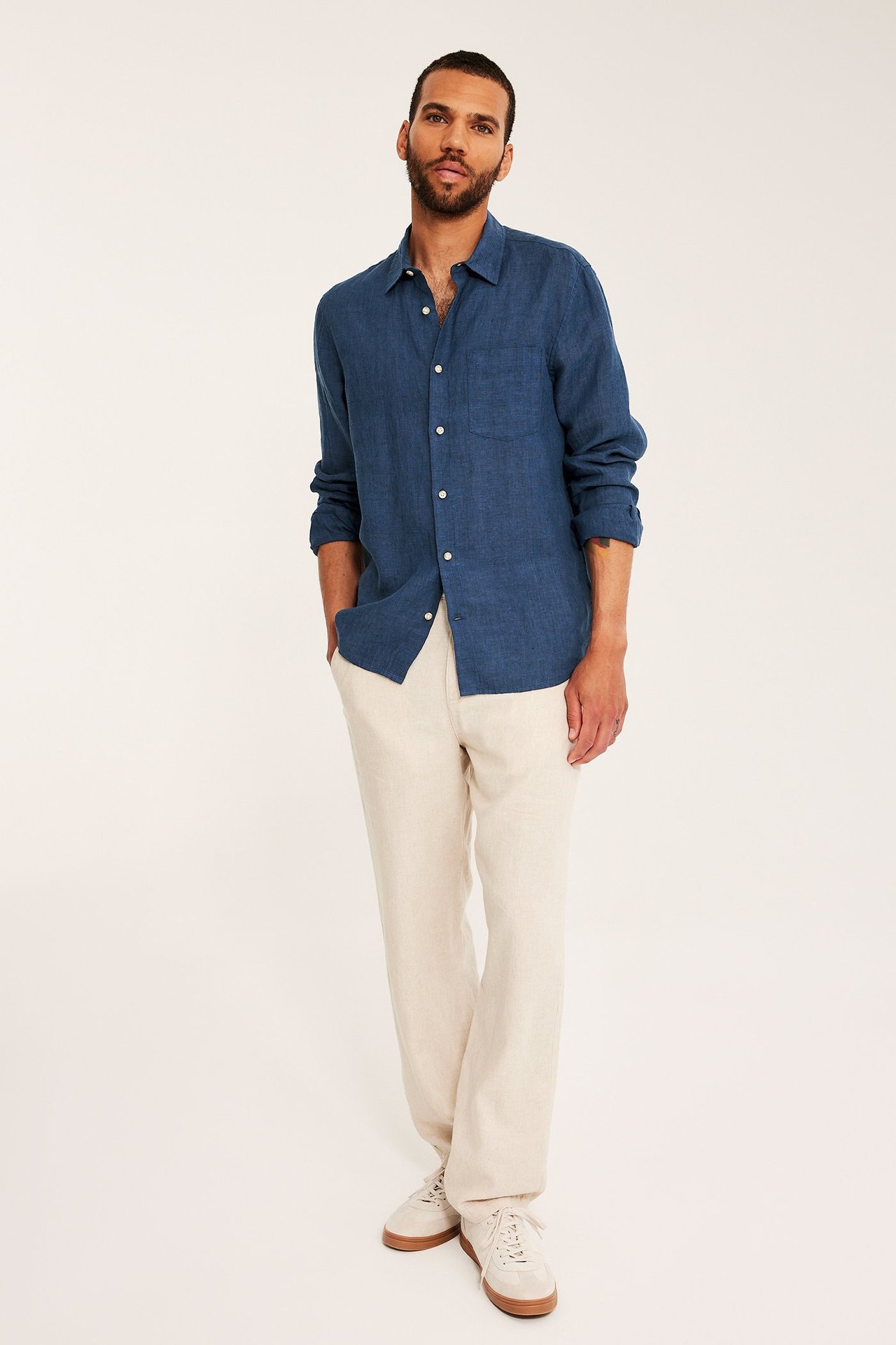Edestäpäin: mies tummansinisessä meleeratussa pellavapaidassa, vaaleanbeigeissä housuissa ja lenkkareissa.
