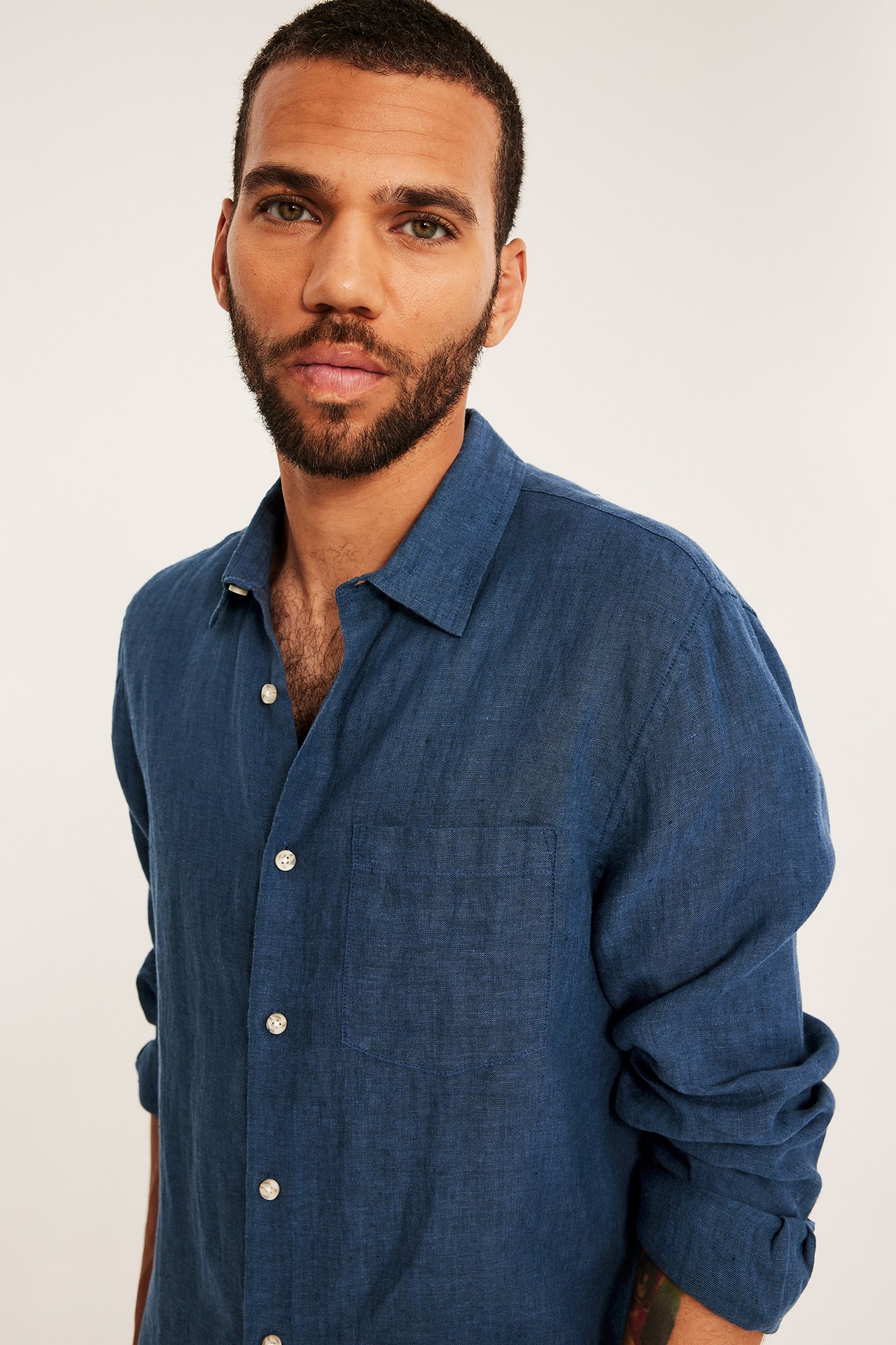 Nærbilde, forfra, av en mann i en mørkeblå melert linskjorte med brystlomme, delvis åpen.