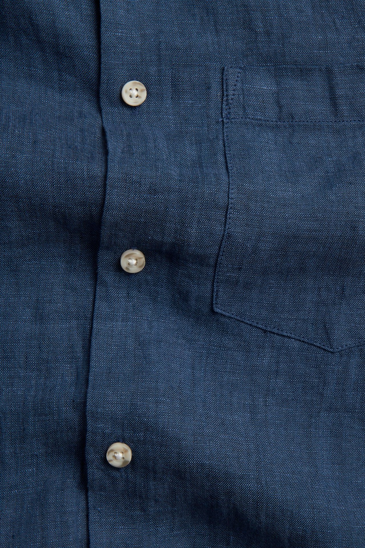 Zbliżenie, przód, granatowej lnianej koszuli melanżowej z jasnymi guzikami i kieszenią.