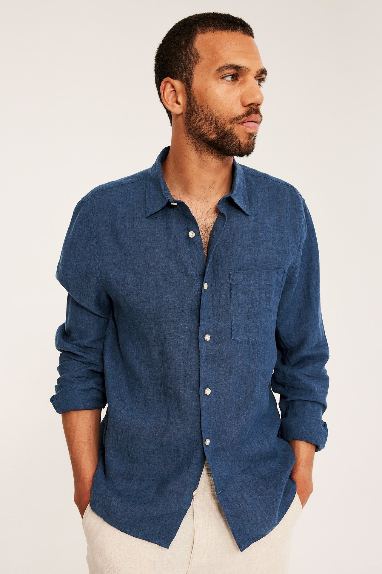 Edestäpäin: mies yllään tummansininen meloitu regular fit pellavapaita rintataskulla ja vaaleabeiget housut.