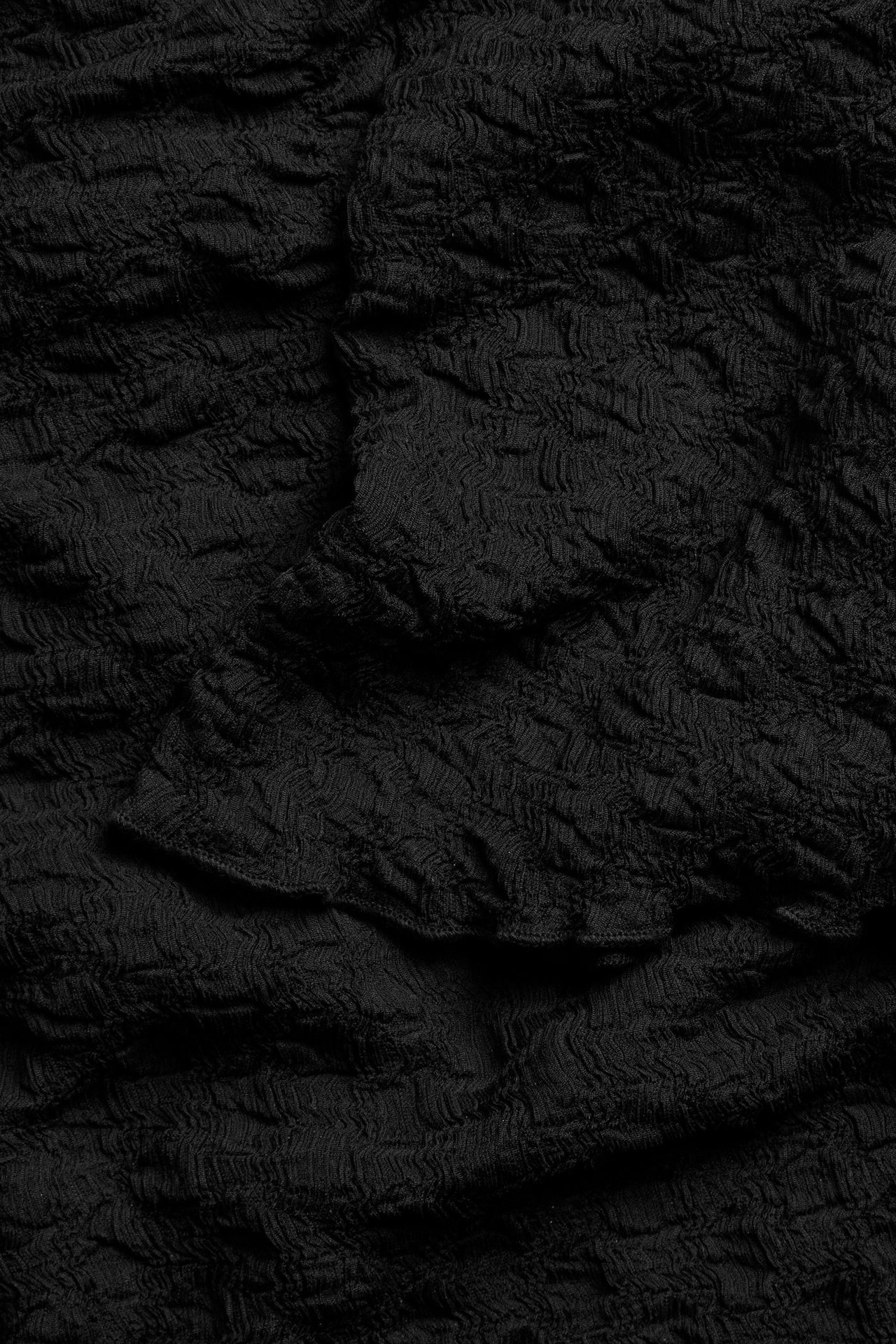 Zbliżenie czarnego, teksturowanego materiału topu z marszczoną powierzchnią i delikatnymi fałdami.