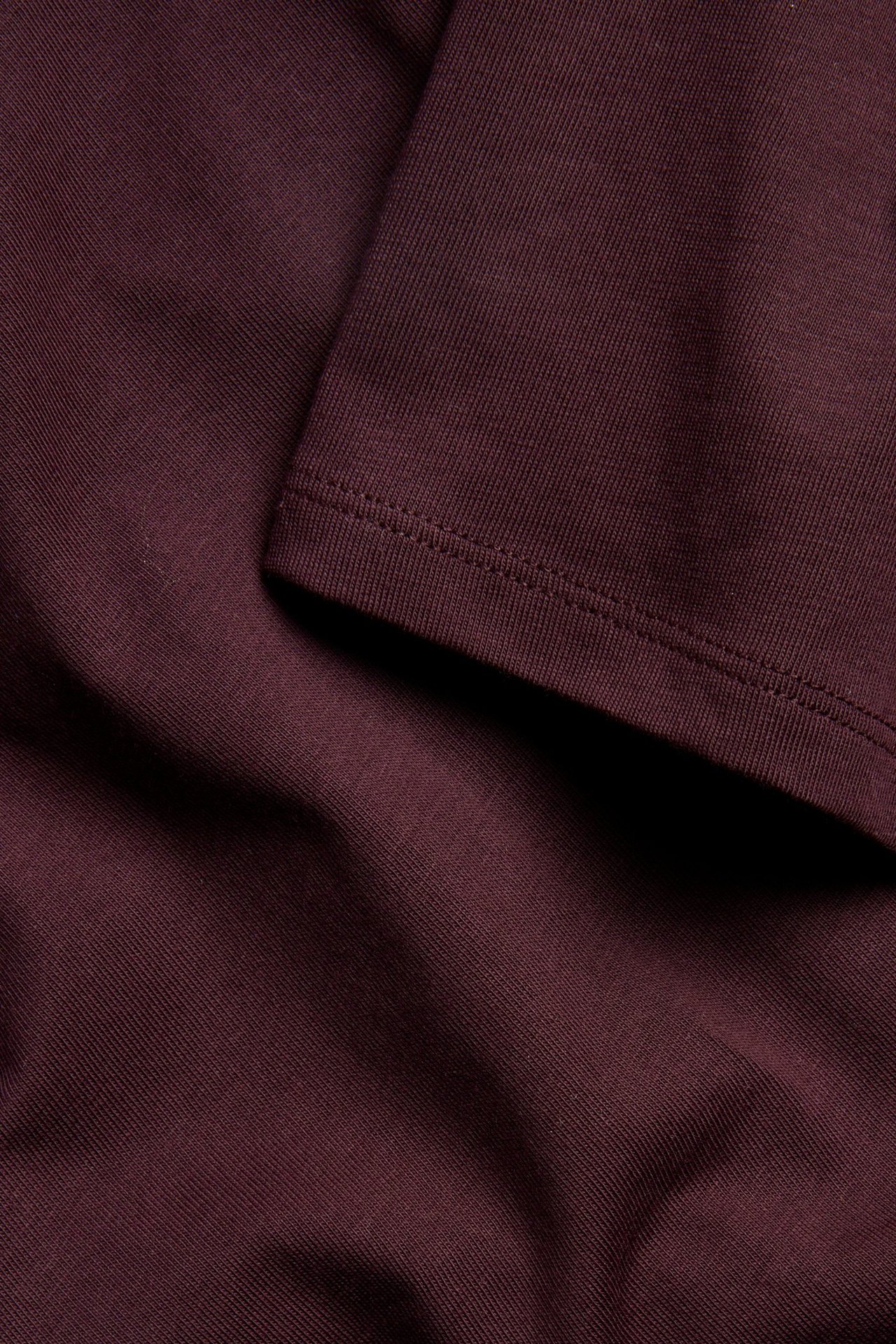 Zbliżenie na bordowy bawełniany T-shirt oversize, ukazujące jednolity złożony materiał z widocznymi szwami.