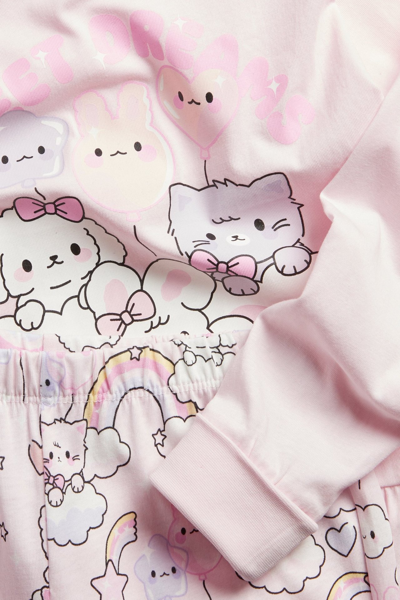 Zbliżenie jasnoróżowej bawełnianej piżamy z długim rękawem, nadrukiem zwierząt, falbankami i składanymi mankietami.