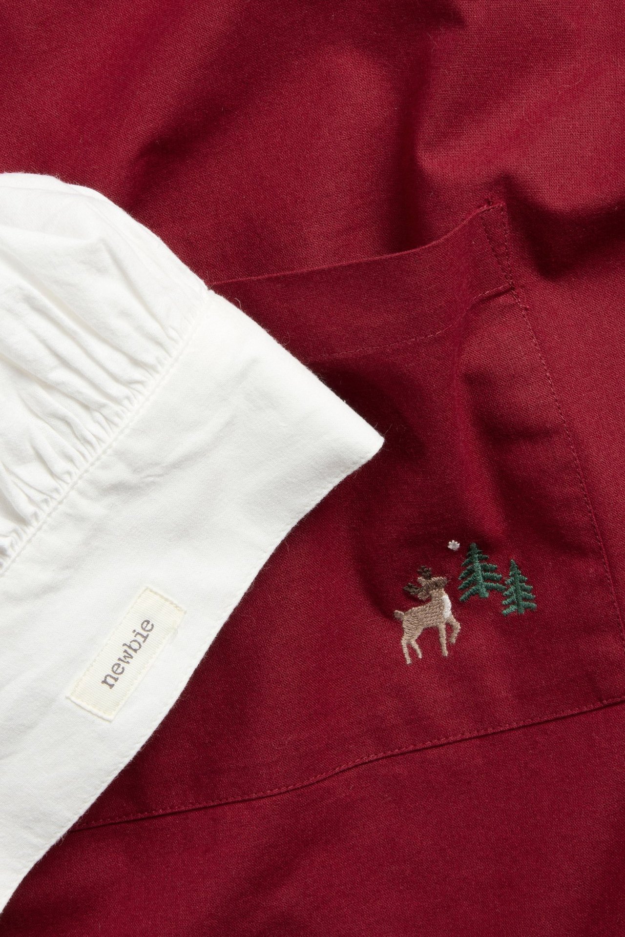 Zbliżenie czerwonego bawełnianego fartucha z haftem renifera i białej, marszczonej czapki piekarza.