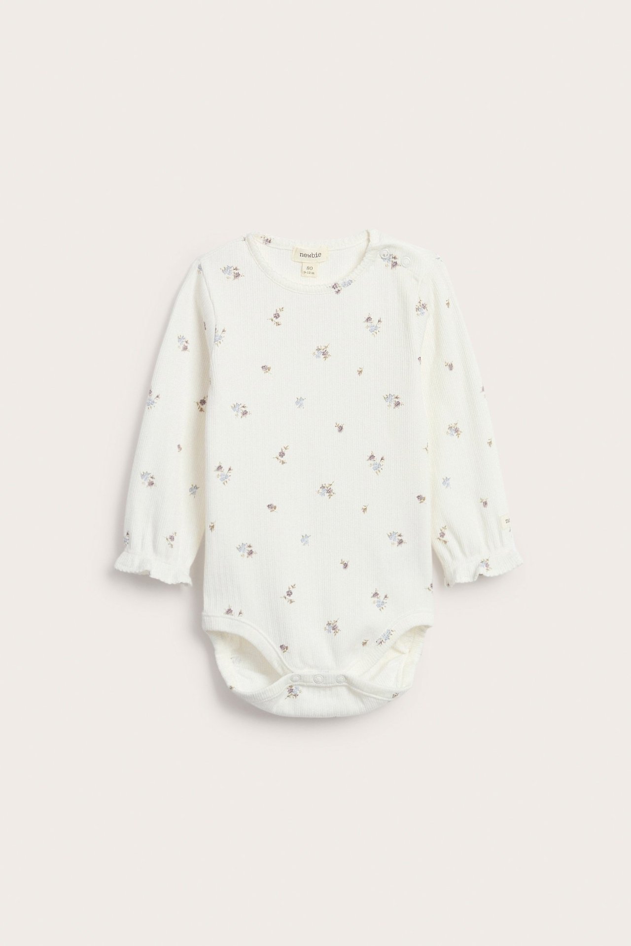 Frontvy av en offwhite ribbet babybody med blomstermønster og volangkanter på ermene.