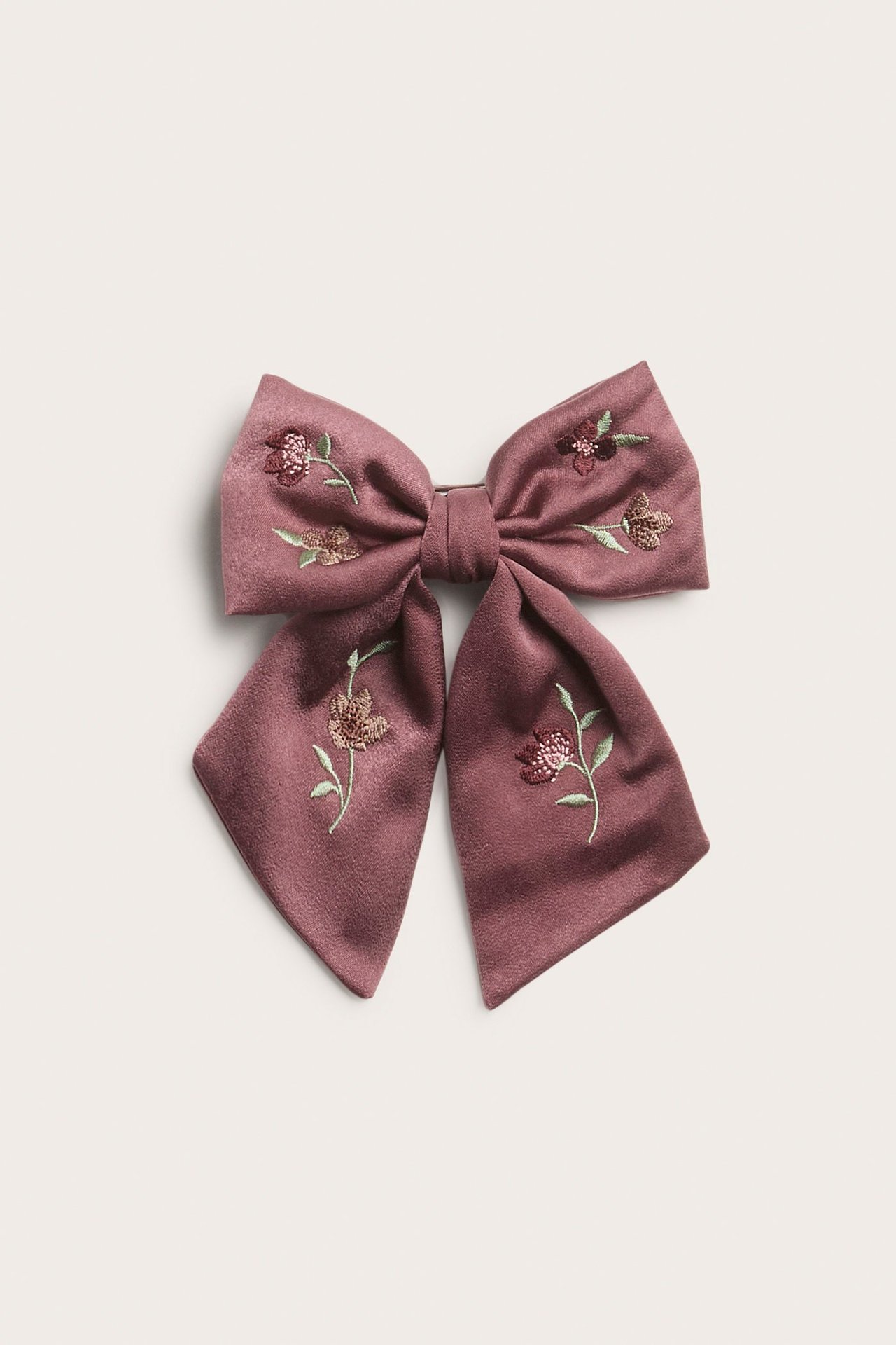 Nærbilde forfra av en mørk rosa satengsløyfe med detaljert blomsterbroderi, festes med metallklemme.