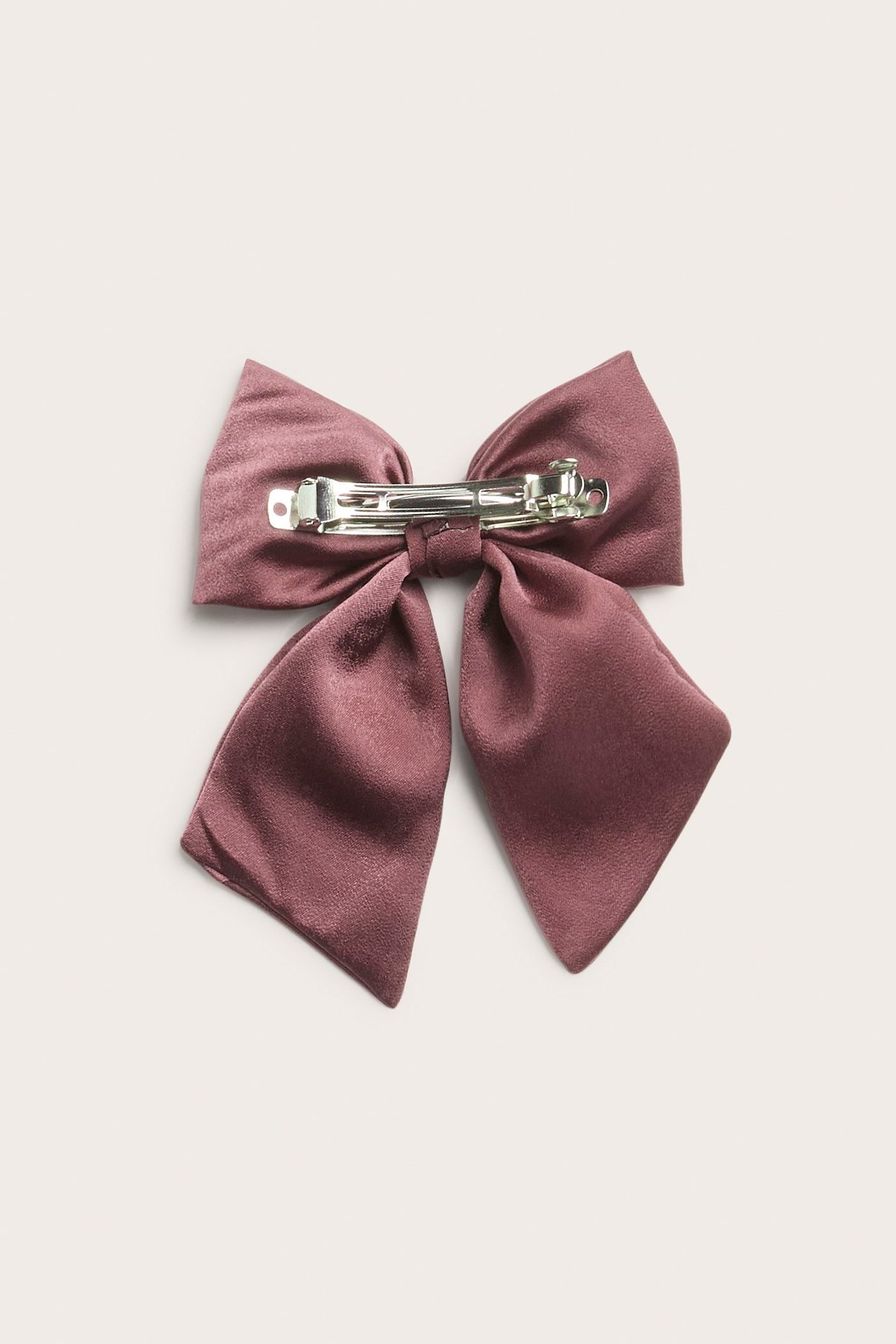 Nærbilde bakfra av en mørk rosa satengsløyfe med metallklemme.