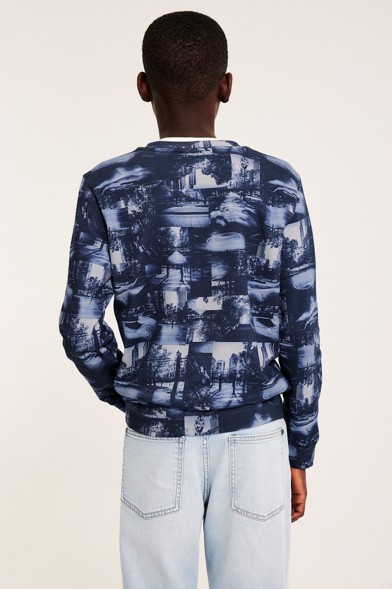 Widok z tyłu dziecka w niebieskiej wzorzystej bawełnianej bluzie dresowej i jasnoniebieskich jeansach.