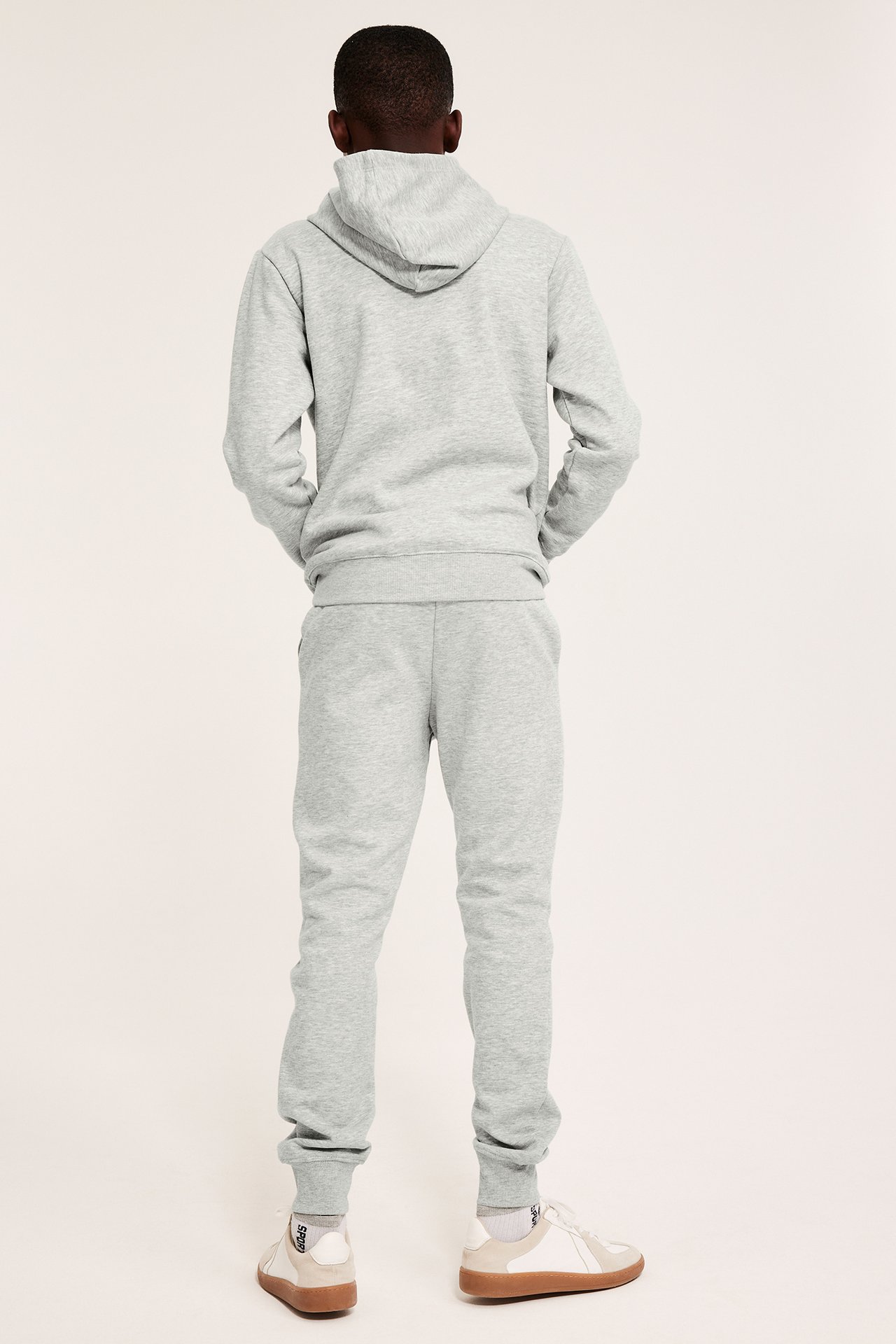 Widok z tyłu dziecka w szarych melanżowych spodniach dresowych, pasującej bluzie, białych skarpetkach i butach.