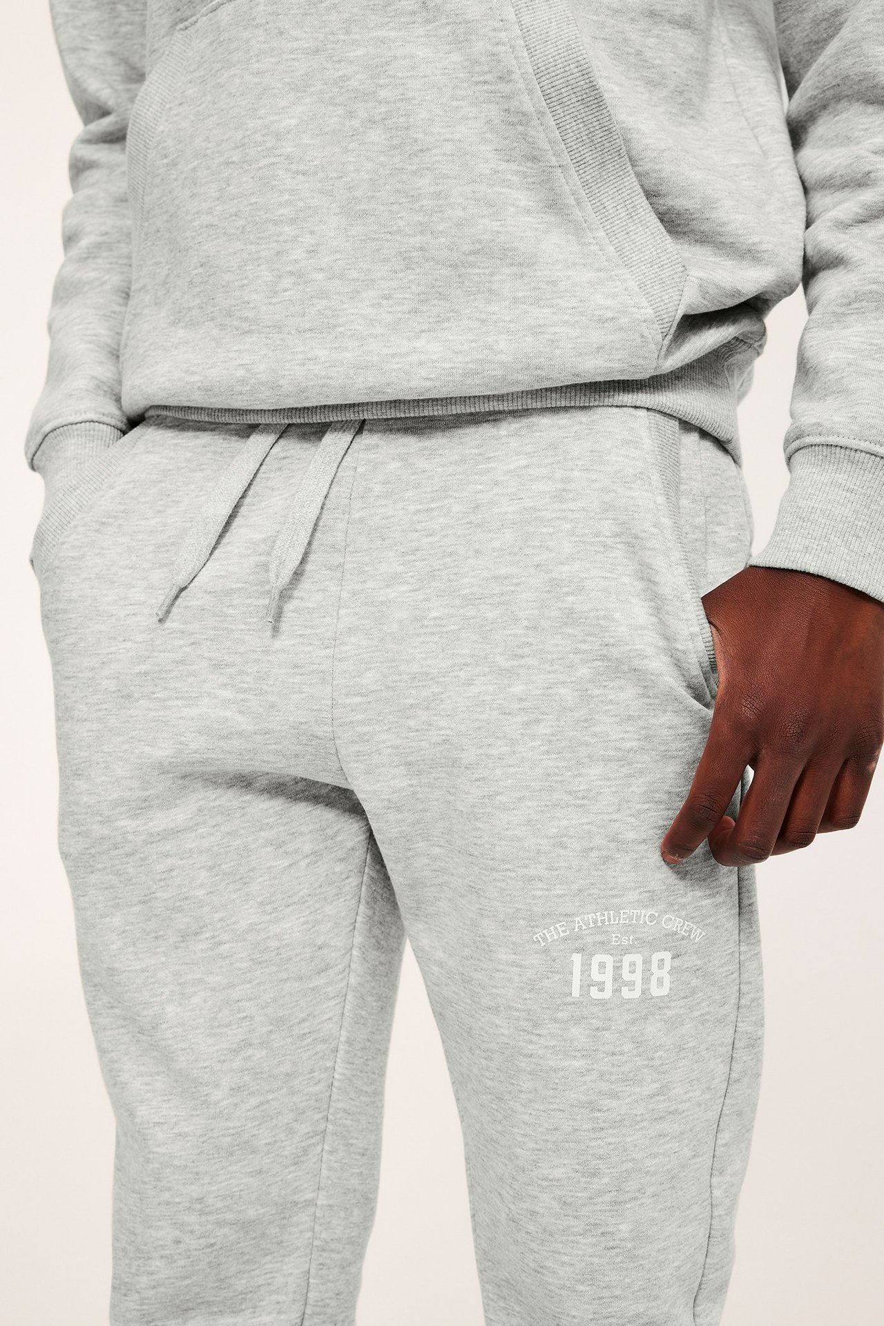 Framifrån: Ett barn bär ljusgråmelerade mjukisbyxor med vitt tryck och en matchande hoodie.